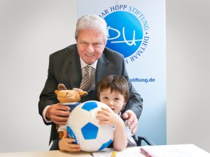 Bei der Pressekonferenz: Dietmar Hopp hatte für Tim, dessen Stoffwechselkrankheit dank Neugeborenenscreening entdeckt und behandelt werden konnte, einen Fußball und Eintrittskarten für den Heidelberger Zoo im Gepäck. Foto: Universitätsklinikum Heidelberg