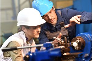 Metal worker teaching trainee on machine use